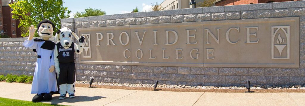 Friar Dom and Huxley, the mascots of Providence College, wave hello in front of the Providence College wall.